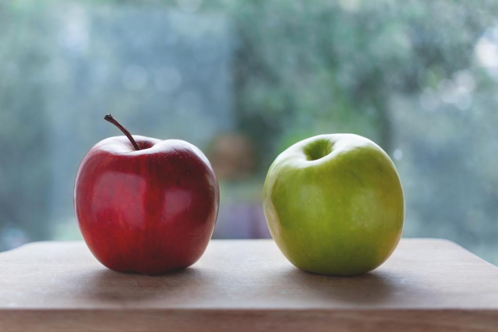 A red apple and a green apple side by side on a table.